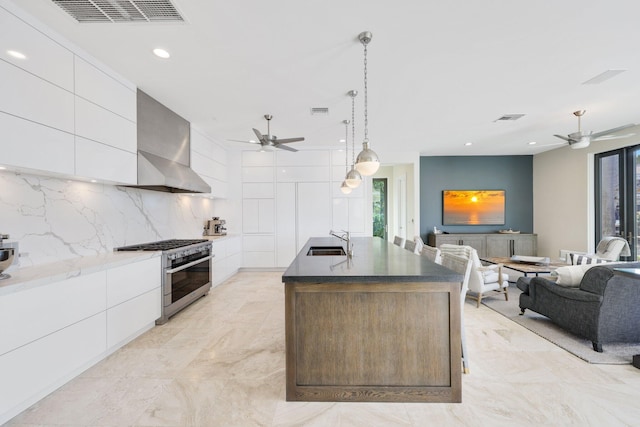 kitchen featuring pendant lighting, sink, white cabinets, high end stainless steel range, and a center island with sink