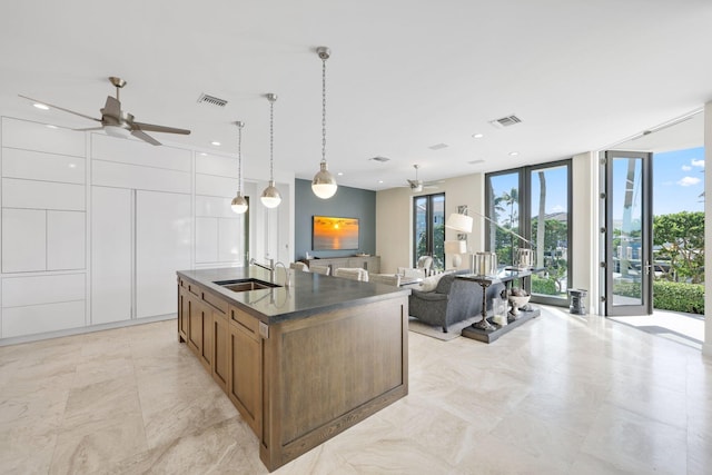 kitchen featuring sink, decorative light fixtures, a wall of windows, ceiling fan, and a kitchen island with sink