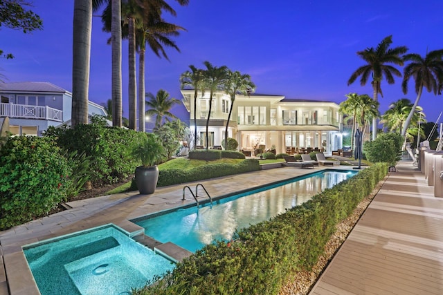 pool at dusk with a patio and an in ground hot tub