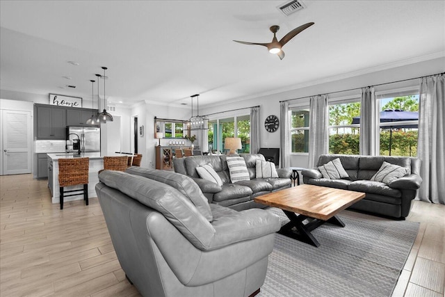 living room with ceiling fan with notable chandelier, ornamental molding, light hardwood / wood-style floors, and a healthy amount of sunlight