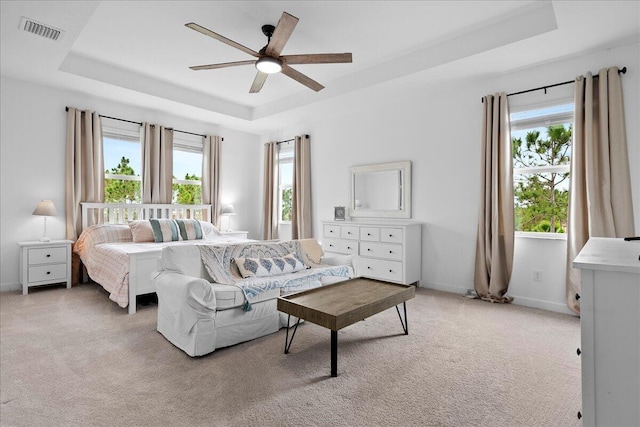 carpeted bedroom with ceiling fan, a tray ceiling, and multiple windows