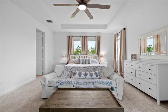 carpeted bedroom with a raised ceiling and ceiling fan