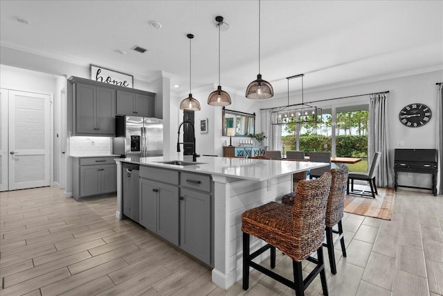 kitchen featuring gray cabinetry, sink, stainless steel appliances, and a center island with sink