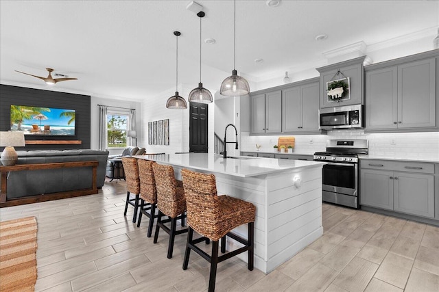 kitchen with sink, gray cabinetry, stainless steel appliances, an island with sink, and a kitchen bar