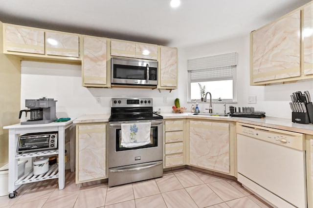 kitchen with stainless steel appliances, light countertops, light brown cabinets, light tile patterned floors, and a sink