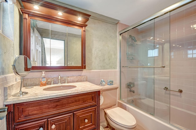 full bathroom featuring tile walls, shower / bath combination with glass door, vanity, ornamental molding, and toilet