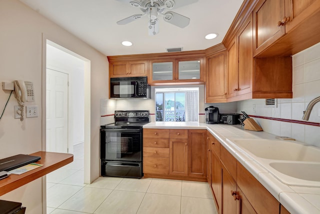 kitchen featuring tile countertops, sink, decorative backsplash, and black appliances