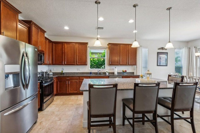 kitchen featuring pendant lighting, appliances with stainless steel finishes, a kitchen island, sink, and a breakfast bar area