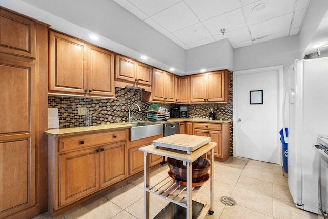 kitchen with a paneled ceiling, white fridge, sink, backsplash, and light tile patterned flooring