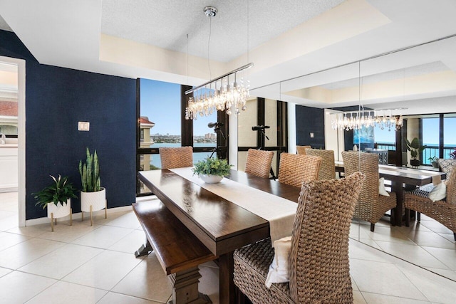 tiled dining area with a notable chandelier, a water view, and a tray ceiling