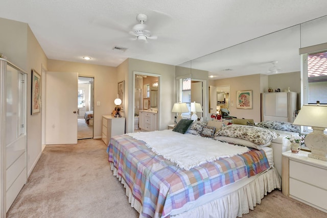 bedroom with ensuite bathroom, light colored carpet, and ceiling fan