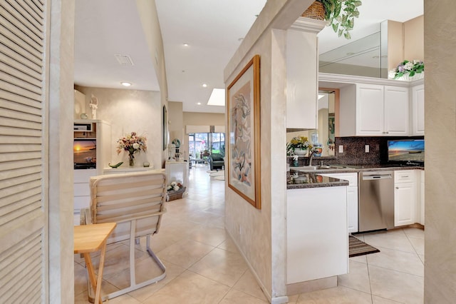 kitchen featuring white cabinetry, light tile patterned floors, stainless steel dishwasher, dark stone counters, and backsplash