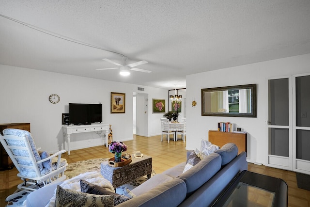 living room featuring ceiling fan with notable chandelier and a textured ceiling