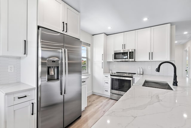 kitchen featuring stainless steel appliances, white cabinetry, light stone countertops, and sink