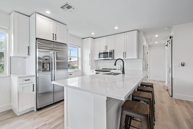 kitchen featuring a kitchen bar, sink, light stone counters, stainless steel appliances, and white cabinets