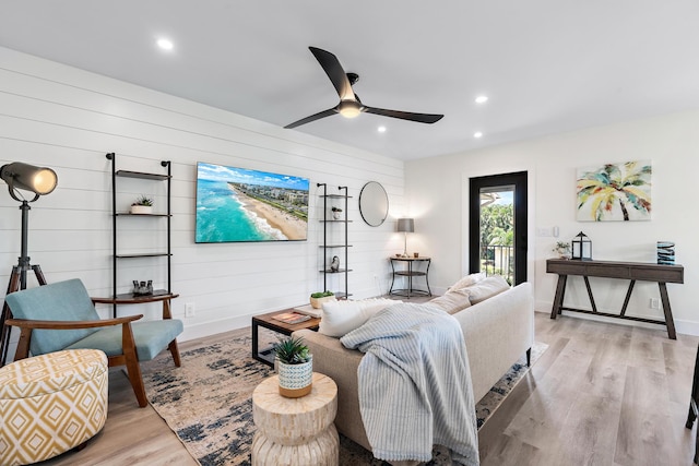 living room featuring ceiling fan, wooden walls, and light hardwood / wood-style floors