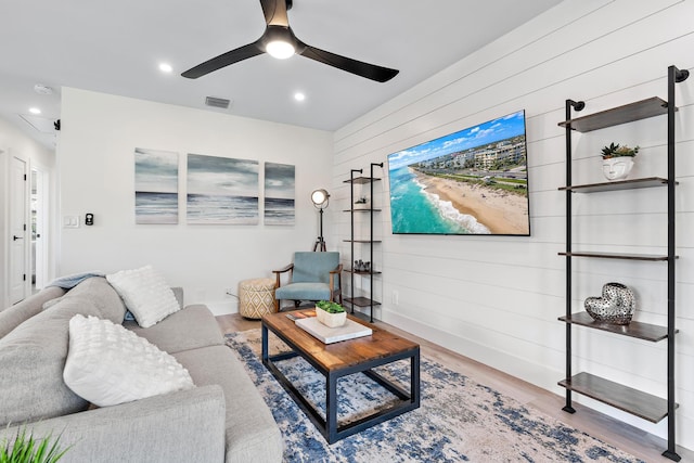 living room featuring wood-type flooring, ceiling fan, and wood walls