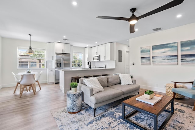 living room with ceiling fan, sink, electric panel, and light hardwood / wood-style floors