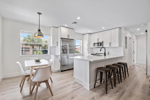 kitchen featuring white cabinetry, appliances with stainless steel finishes, kitchen peninsula, pendant lighting, and light hardwood / wood-style floors