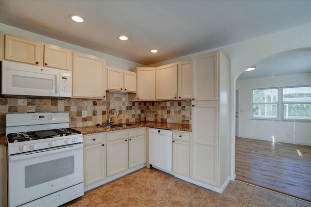 kitchen featuring light tile patterned floors, sink, white appliances, decorative backsplash, and dark stone counters