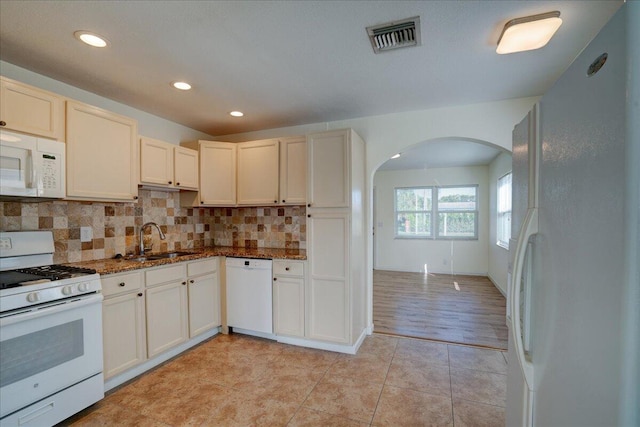 kitchen with dark stone countertops, sink, white appliances, and decorative backsplash