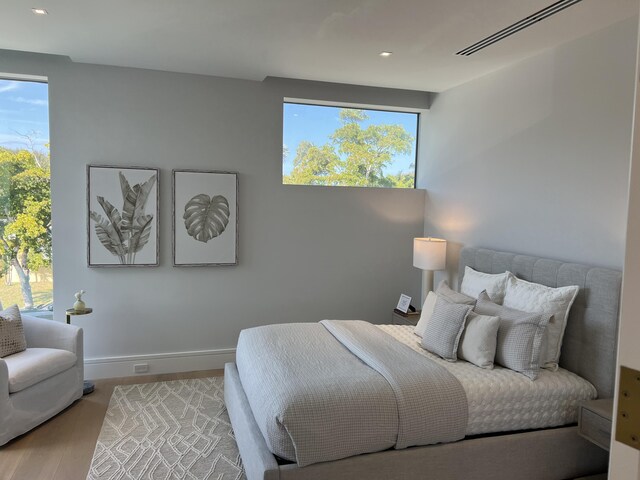 bedroom with baseboards, multiple windows, visible vents, and wood finished floors