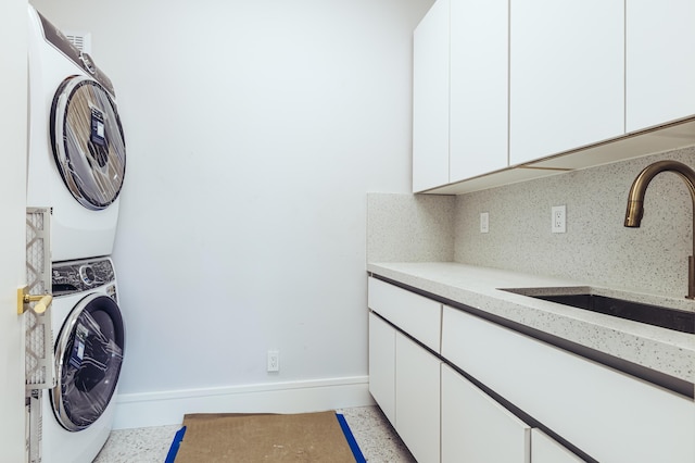 laundry room with baseboards, a sink, cabinet space, and stacked washer / drying machine