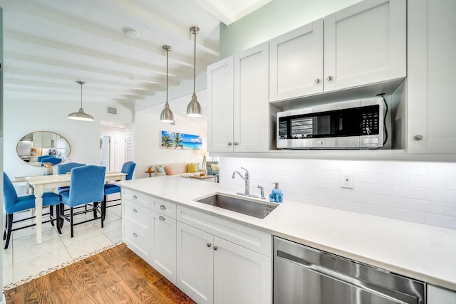 kitchen with wood-type flooring, sink, white cabinets, decorative light fixtures, and stainless steel appliances