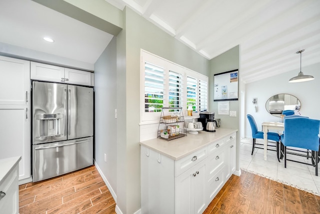 kitchen with pendant lighting, white cabinets, stainless steel fridge with ice dispenser, and vaulted ceiling