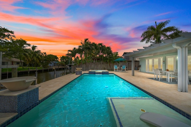 pool at dusk with an in ground hot tub, a patio area, french doors, and a water view