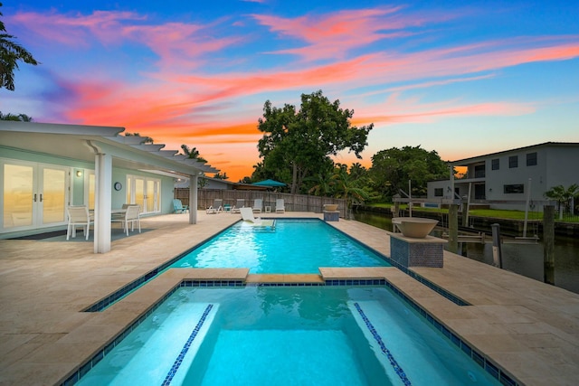 pool at dusk with an in ground hot tub, french doors, and a patio