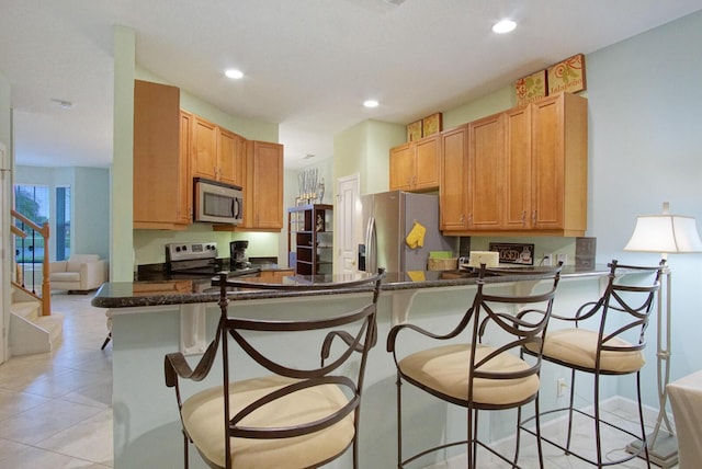 kitchen featuring stainless steel appliances, dark stone counters, kitchen peninsula, light tile patterned flooring, and a breakfast bar area