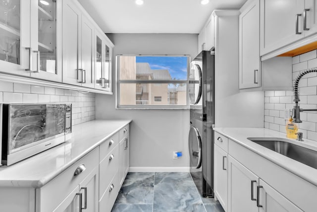 laundry area featuring stacked washer / drying machine, sink, and cabinets