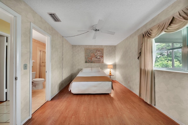 bedroom with ceiling fan, connected bathroom, light hardwood / wood-style floors, and a textured ceiling