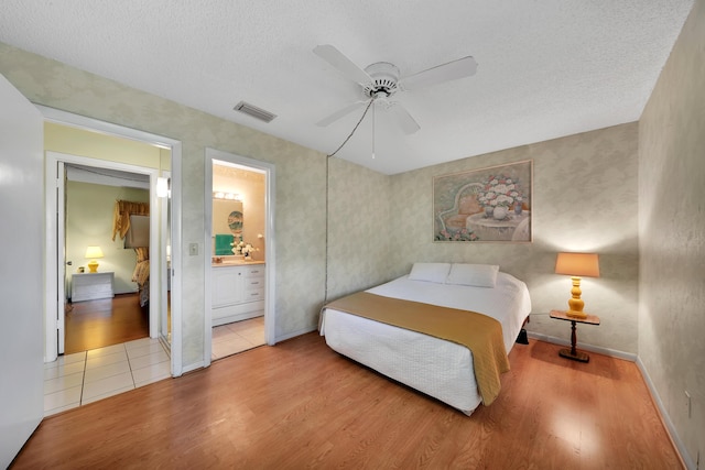 bedroom featuring ceiling fan, connected bathroom, a textured ceiling, and light wood-type flooring