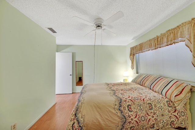 bedroom featuring ceiling fan, light hardwood / wood-style floors, and a textured ceiling