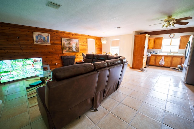 tiled living room featuring sink, ceiling fan, wooden walls, and a textured ceiling