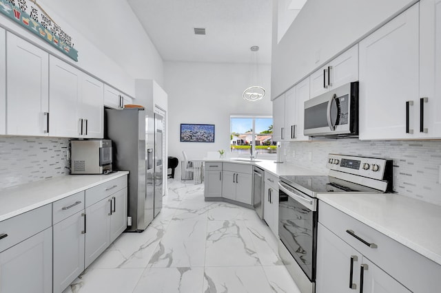 kitchen with pendant lighting, appliances with stainless steel finishes, a towering ceiling, tasteful backsplash, and sink