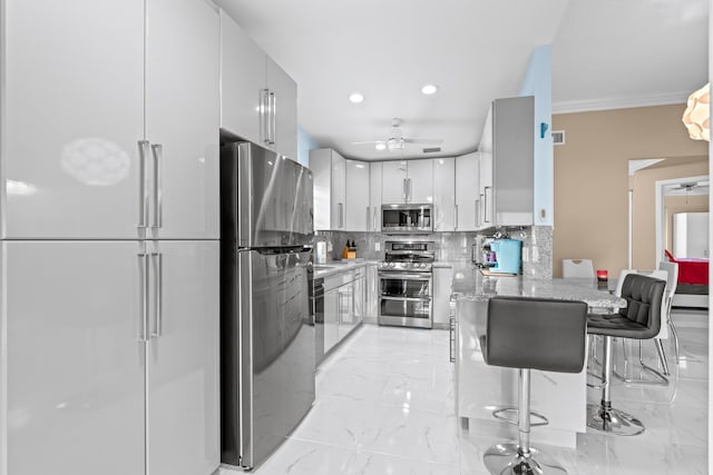 kitchen featuring white cabinets, stainless steel appliances, decorative backsplash, a kitchen breakfast bar, and ceiling fan