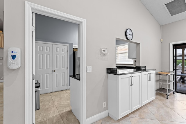 kitchen featuring light tile patterned flooring, a healthy amount of sunlight, white cabinetry, and lofted ceiling