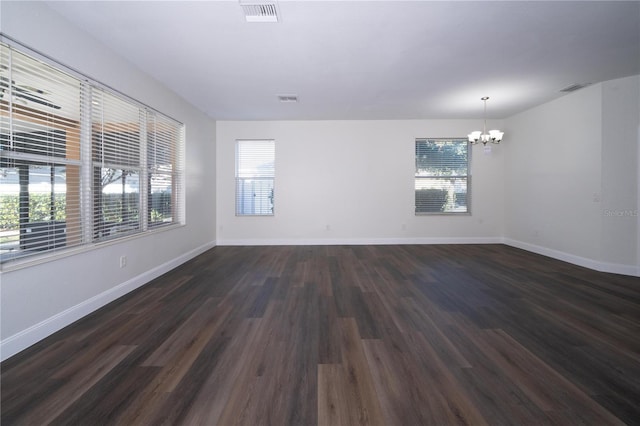 empty room with dark wood-type flooring and a notable chandelier