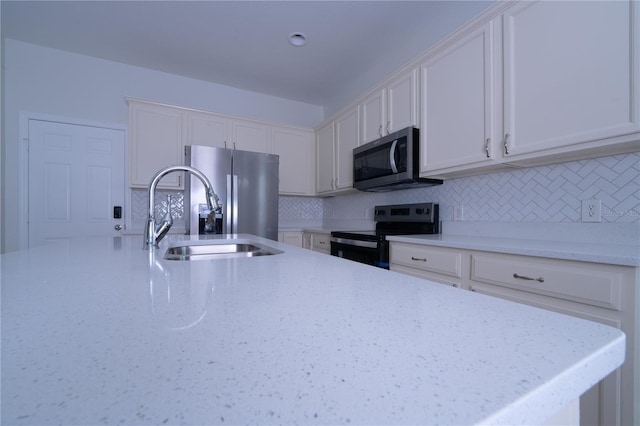 kitchen with sink, white cabinetry, backsplash, stainless steel appliances, and light stone countertops