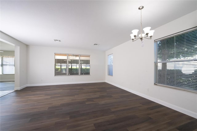 spare room with dark hardwood / wood-style flooring and an inviting chandelier