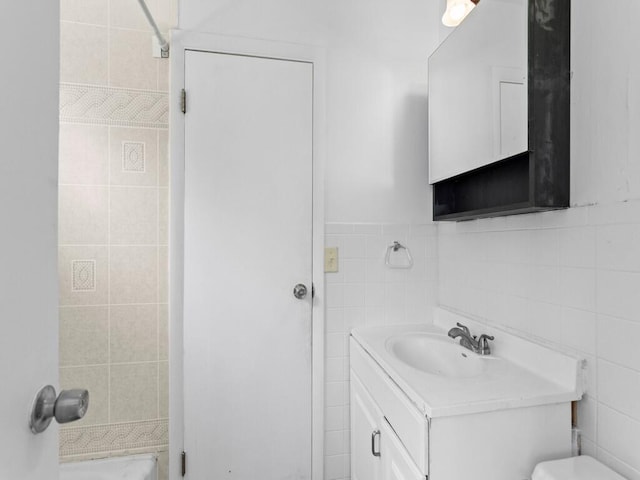 bathroom featuring vanity, toilet, tile walls, and a shower