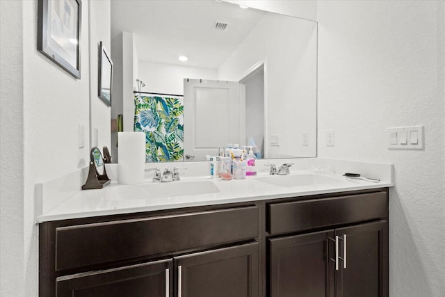 full bathroom with a textured wall, visible vents, a sink, and double vanity