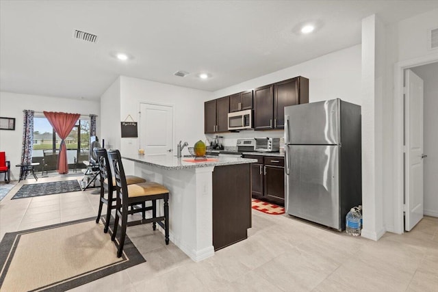 kitchen featuring a breakfast bar, visible vents, appliances with stainless steel finishes, a sink, and dark brown cabinets