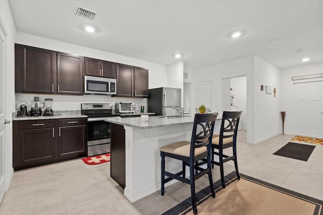 kitchen with a breakfast bar area, visible vents, appliances with stainless steel finishes, dark brown cabinets, and an island with sink