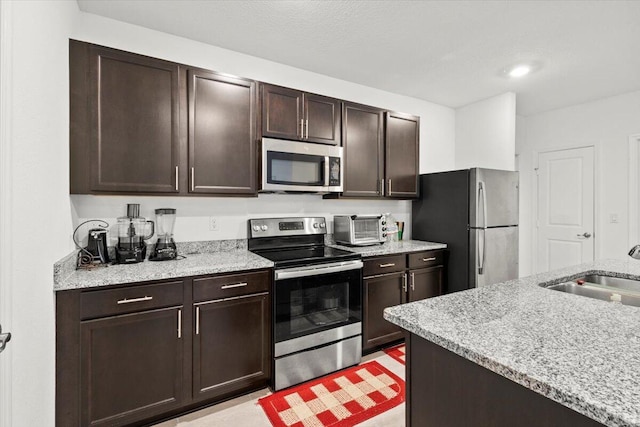 kitchen with dark brown cabinetry, a toaster, appliances with stainless steel finishes, and a sink