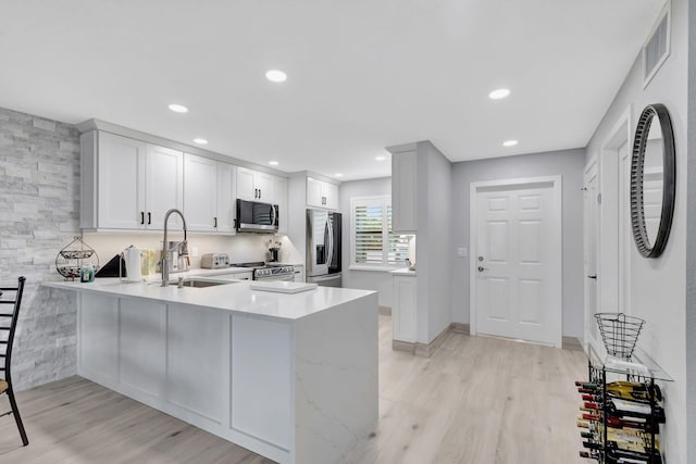 kitchen featuring sink, light wood-type flooring, appliances with stainless steel finishes, kitchen peninsula, and white cabinets