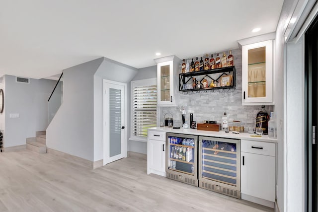 bar with wine cooler, backsplash, white cabinets, and light wood-type flooring